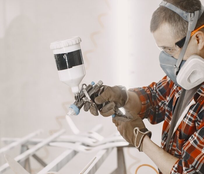 Carpenter in his paint room spraying a piece of wood
